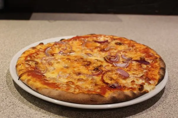 Eine appetitliche Pizza auf einem weissen Teller, mit geschmolzenem Käse und frischen Zutaten.